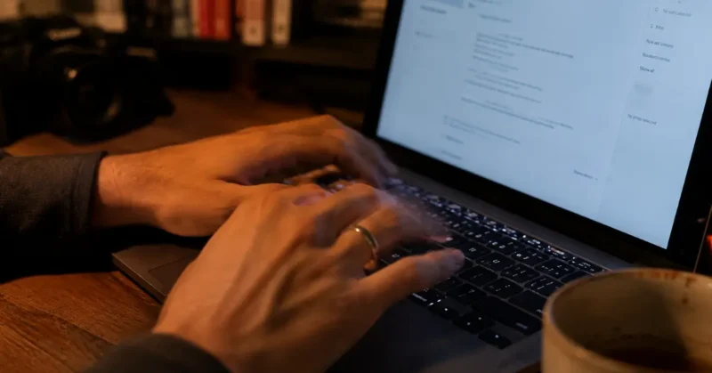 Person typing AI video creation prompts on laptop keyboard with coffee cup beside them